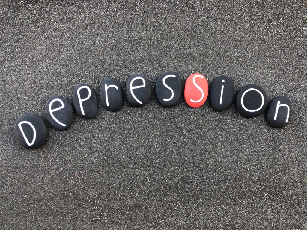 Depression text composed with black and red stones over black volcanic sand