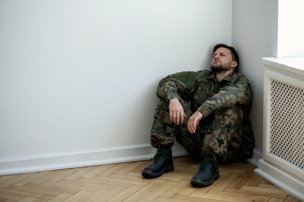 Un militar deprimido con uniforme sentado en una esquina de un ro