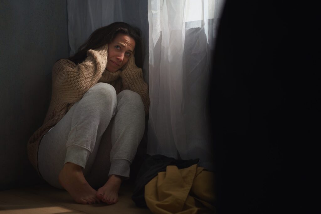 Une femme effrayée s'assoit sur le sol et se couvre la tête par crainte de violences domestiques